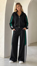 Front full view of woman wearing black 2-piece wide leg tracksuit with green and white side stripes