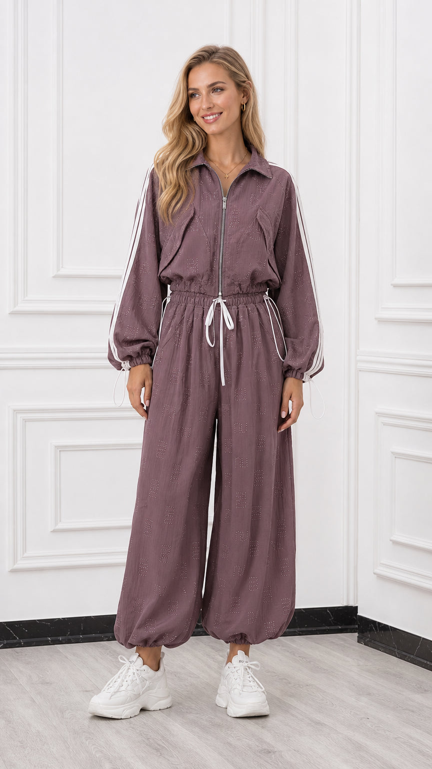 Front view of woman wearing a mauve long sleeve zip-up track jumpsuit with white side stripes