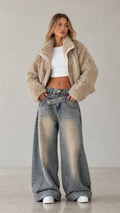 Front view of woman wearing beige cropped faux shearling teddy zip jacket with wide leg jeans