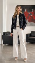 Woman wearing Navy embellished floral zip-up jacket with white trousers, front view