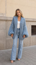 Front view of woman wearing slate blue chunky knit cardigan with balloon sleeves and light wash jeans