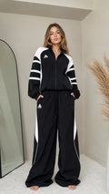 Front full-length view of woman wearing black retro colorblock tracksuit set with wide leg pants