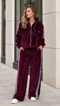 Front view of woman wearing burgundy velour zip-up hoodie and wide-leg tracksuit set with side stripes