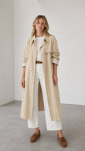Front full view of woman wearing beige trench coat with white pants and loafers