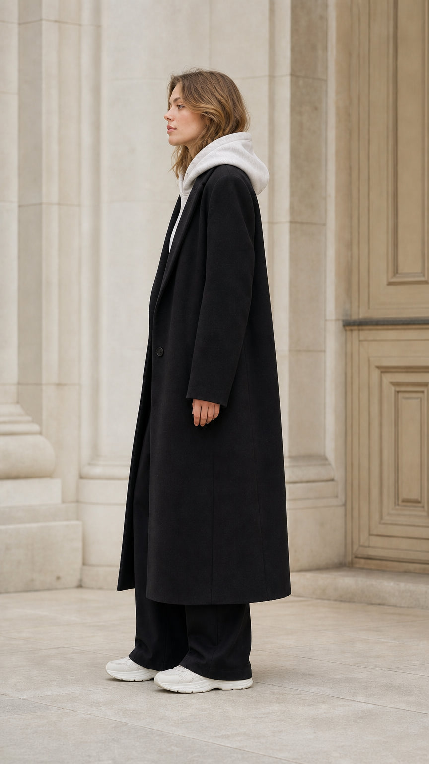 Side profile of model in full-length black tailored maxi overcoat