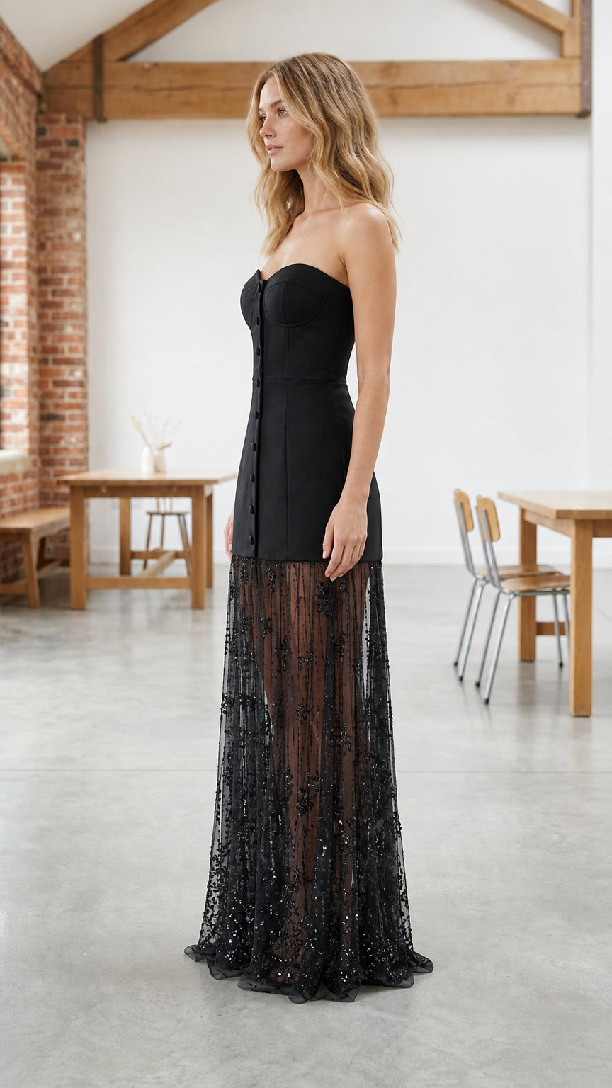 Side profile view of woman modeling black bustier evening dress with embellished mesh skirt