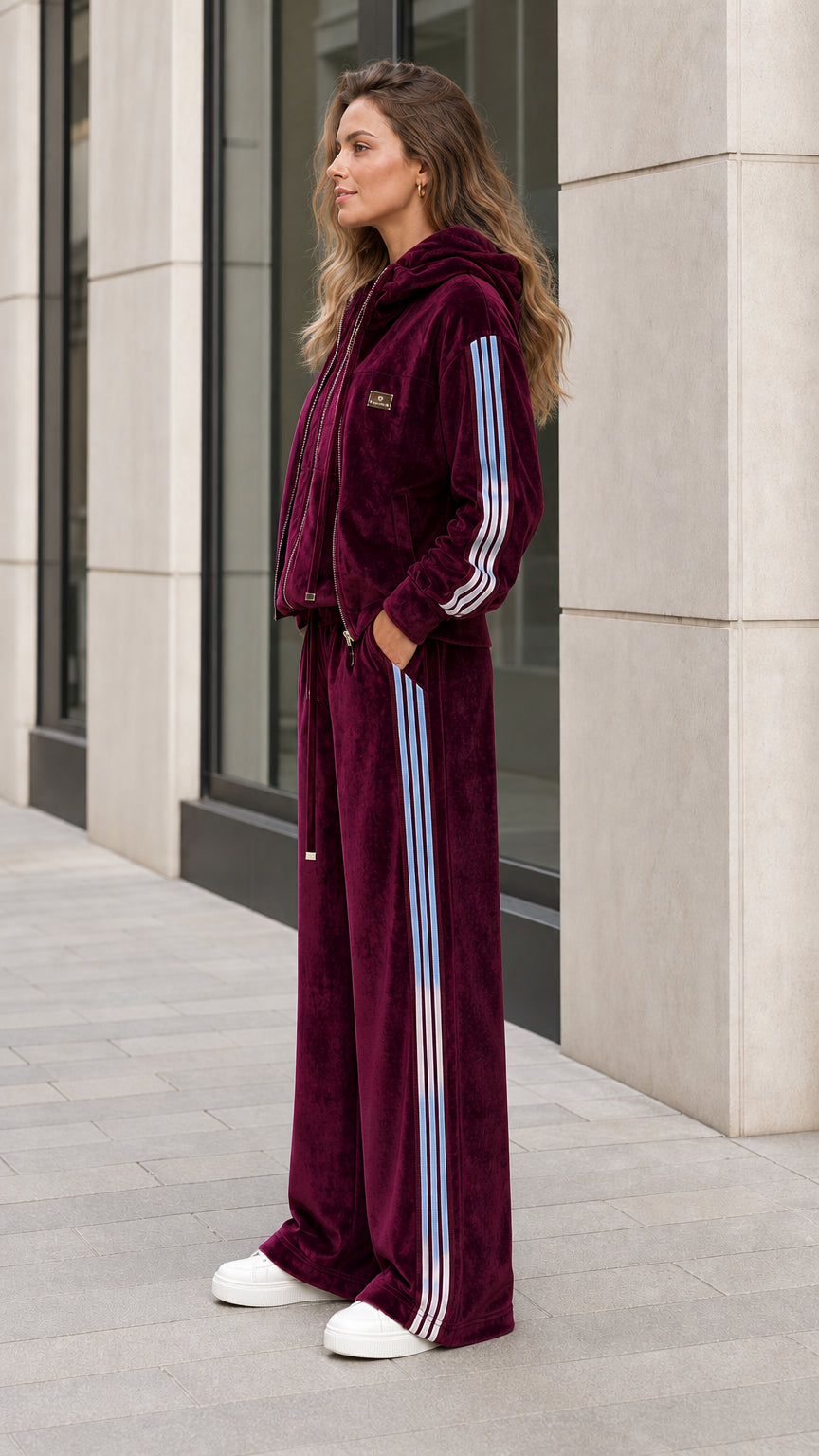 Side angle view of woman in burgundy velvet tracksuit showing contrast sleeve and pant stripes