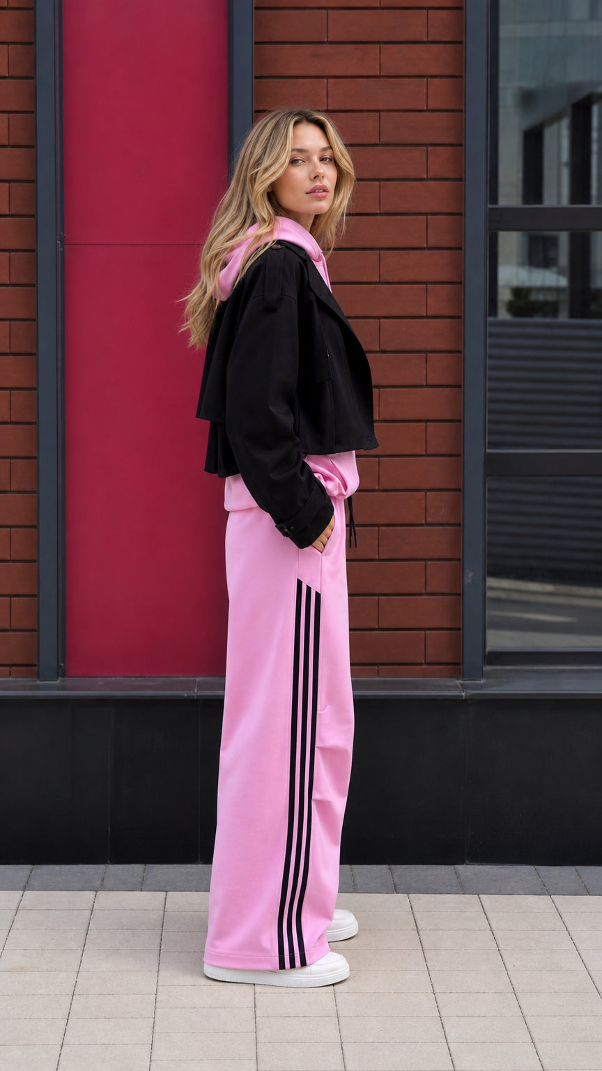 Side profile of pink tracksuit set with black three-stripe detail along pants