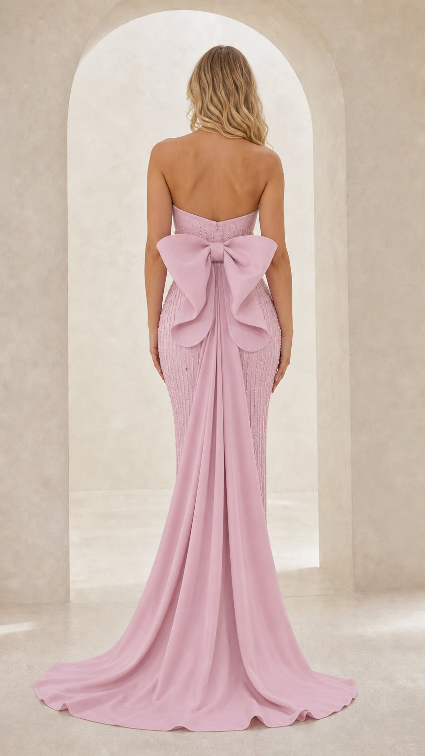 Back view of blush pink strapless evening gown featuring large structured bow and flowing train