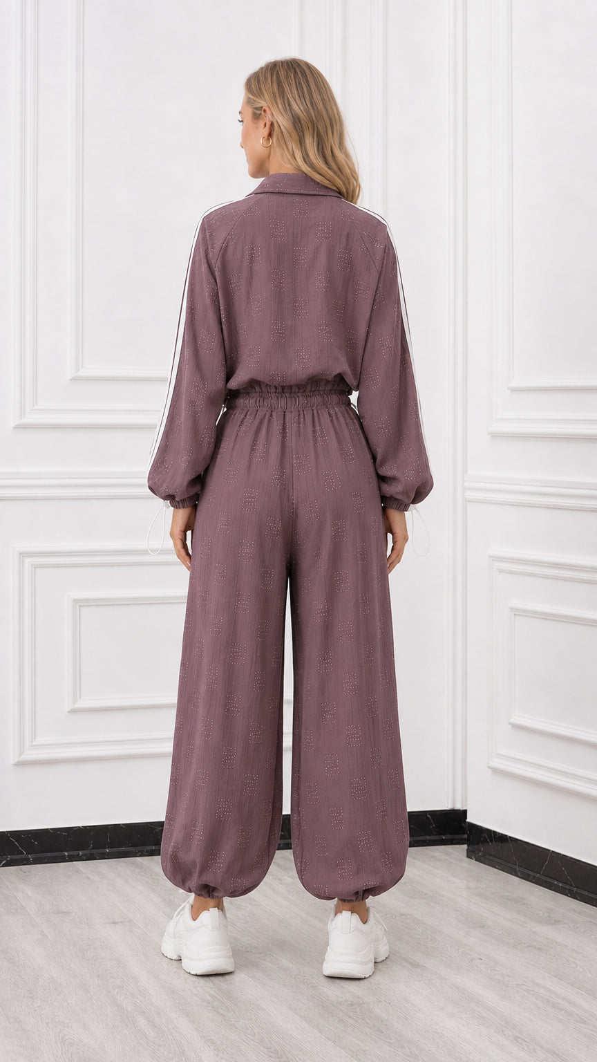 Back view of woman wearing a mauve relaxed fit track jumpsuit with elastic waist