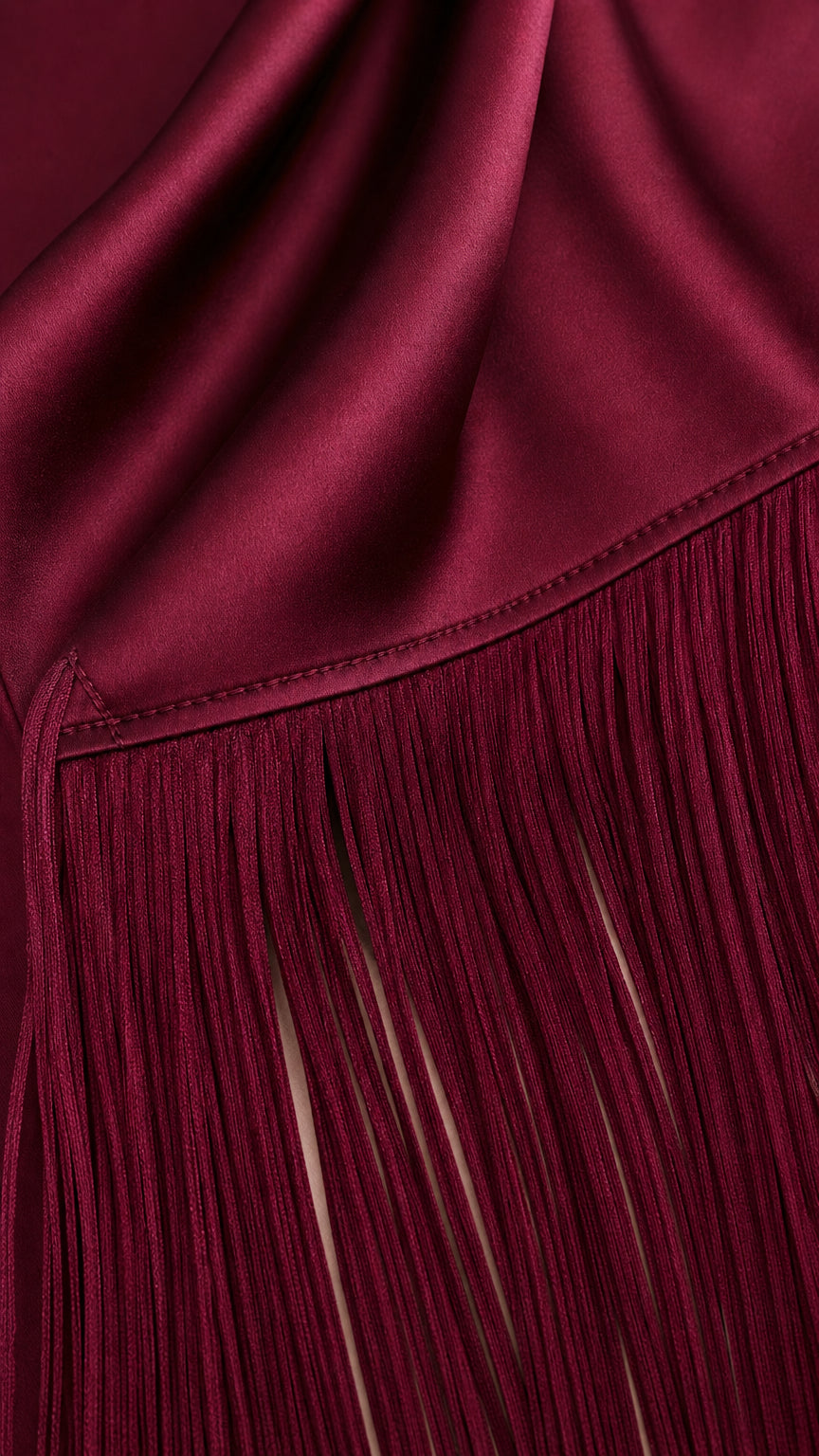 Close-up detail of burgundy satin fabric seam and fine fringe trim
