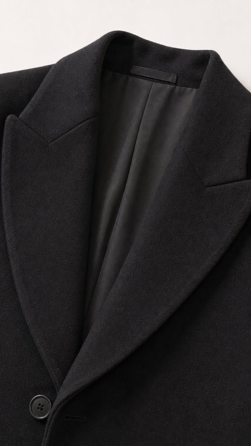 Close-up of black tailored coat notched lapel, button, and smooth lining