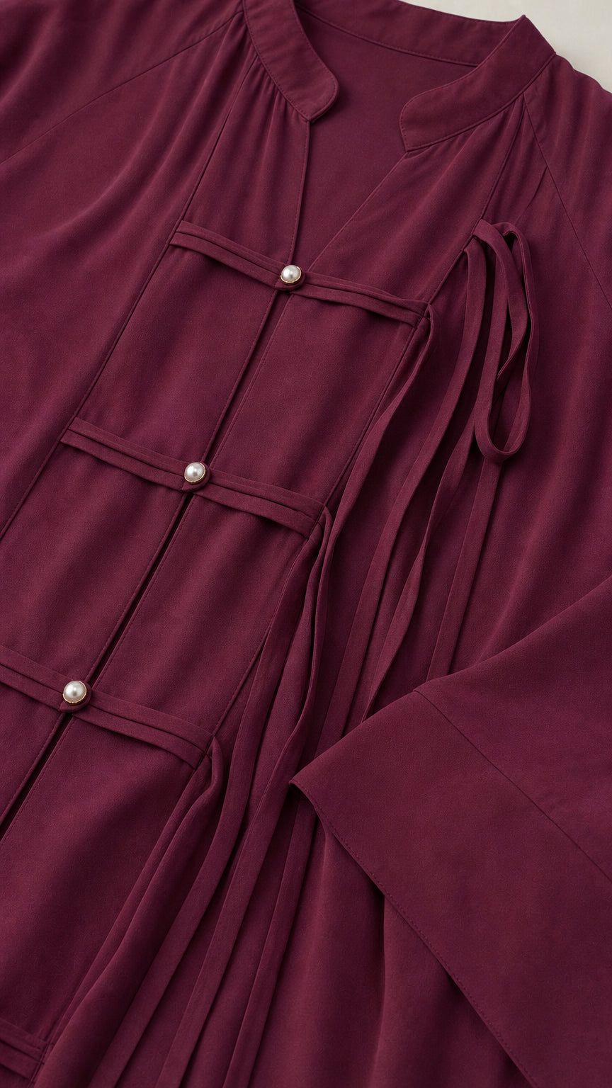 Close-up detail of burgundy tunic showing pearl buttons and frog strap closures